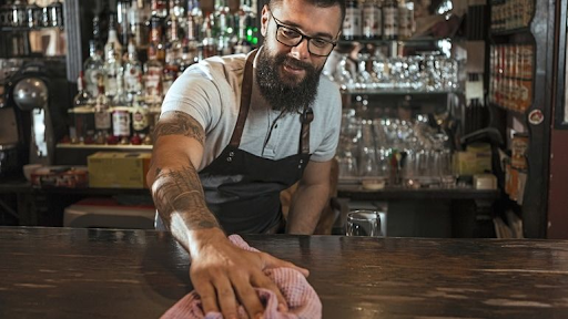 Man in glasses wiping the bar table with a pink cloth