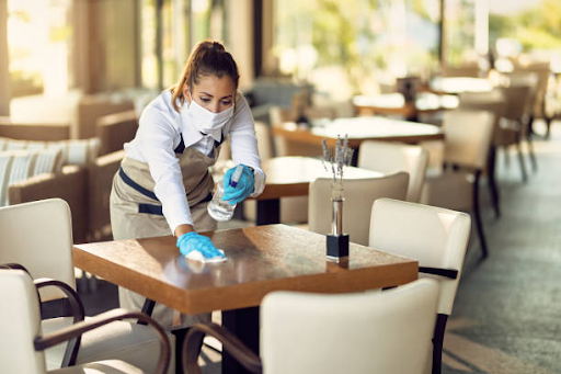 Woman in a mask cleaning a table with a disinfectant spray and a cloth